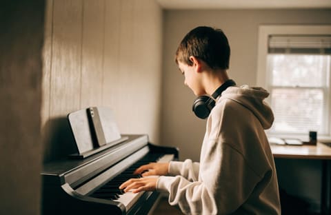 A teenager at a digital keyboard with headphones around the neck, seen from the side