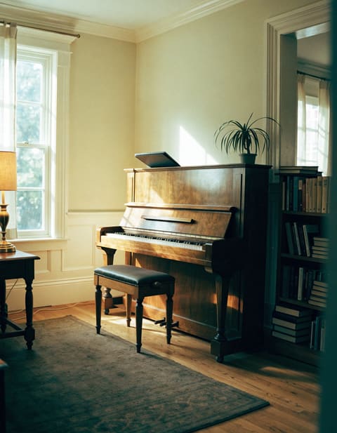 An upright piano in a bright living room in late-afternoon light